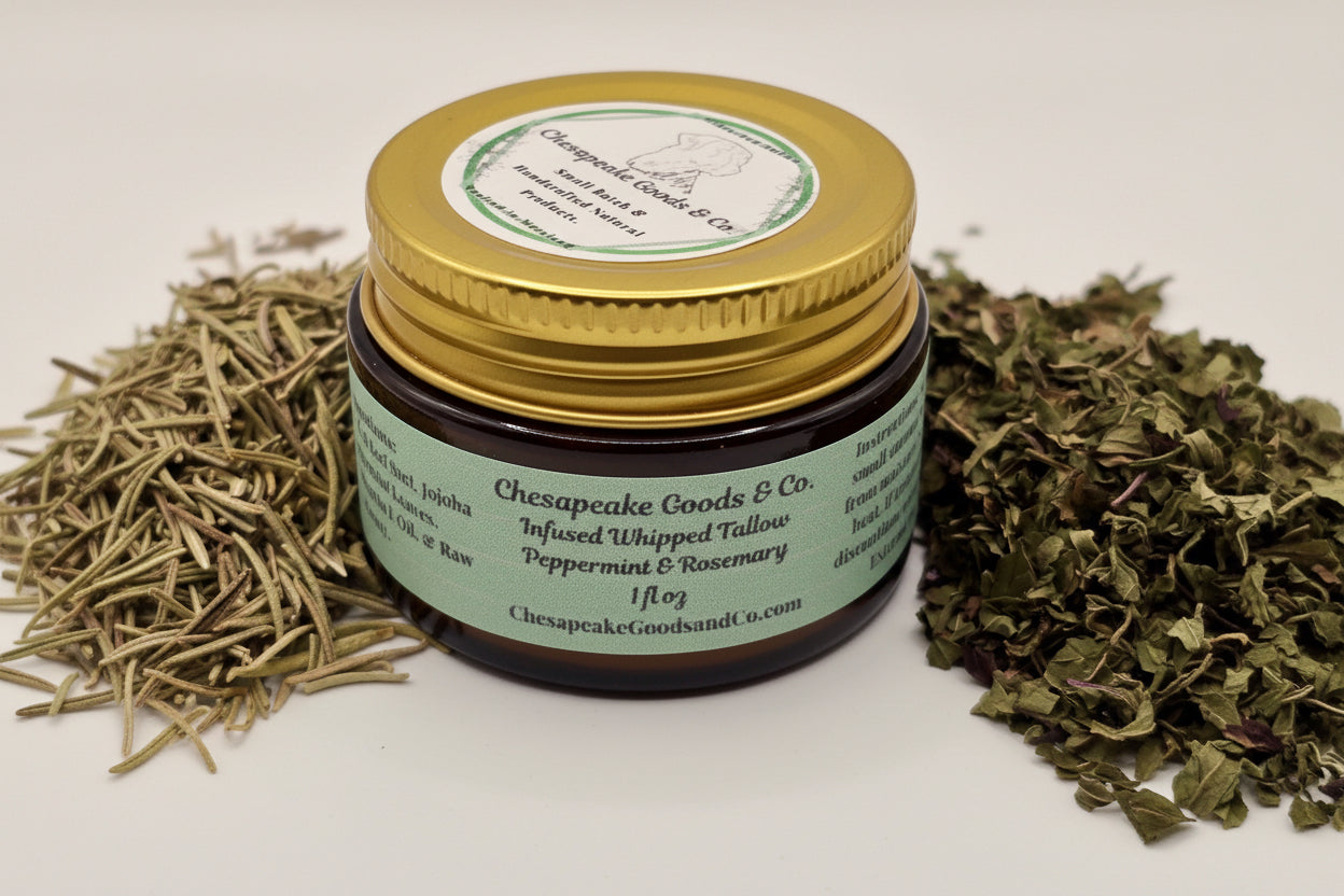 A jar of Chesapeake Goods & Co. infused whipped tallow, peppermint & rosemary, is displayed with dried herbs to highlight its natural ingredients.
