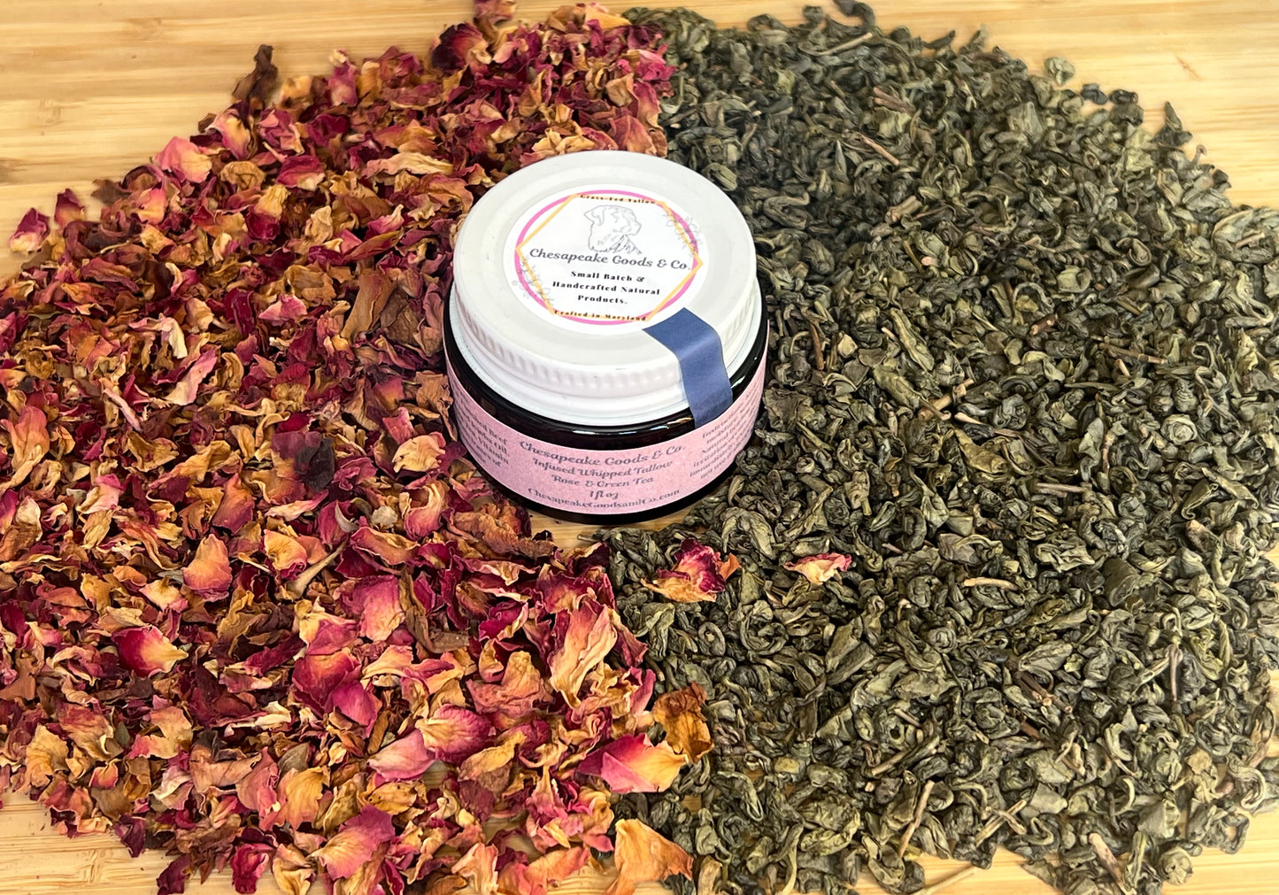 1 oz amber glass jar with a pink wrap label and white top, surrounded by dried green tea leaves and dried rose petals on a wooden surface.