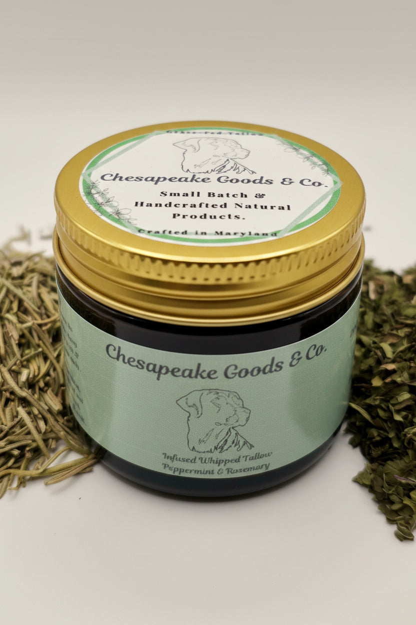 Chesapeake Goods & Co. displays their handcrafted, natural, peppermint and rosemary infused whipped tallow in a jar surrounded by rosemary and mint.
