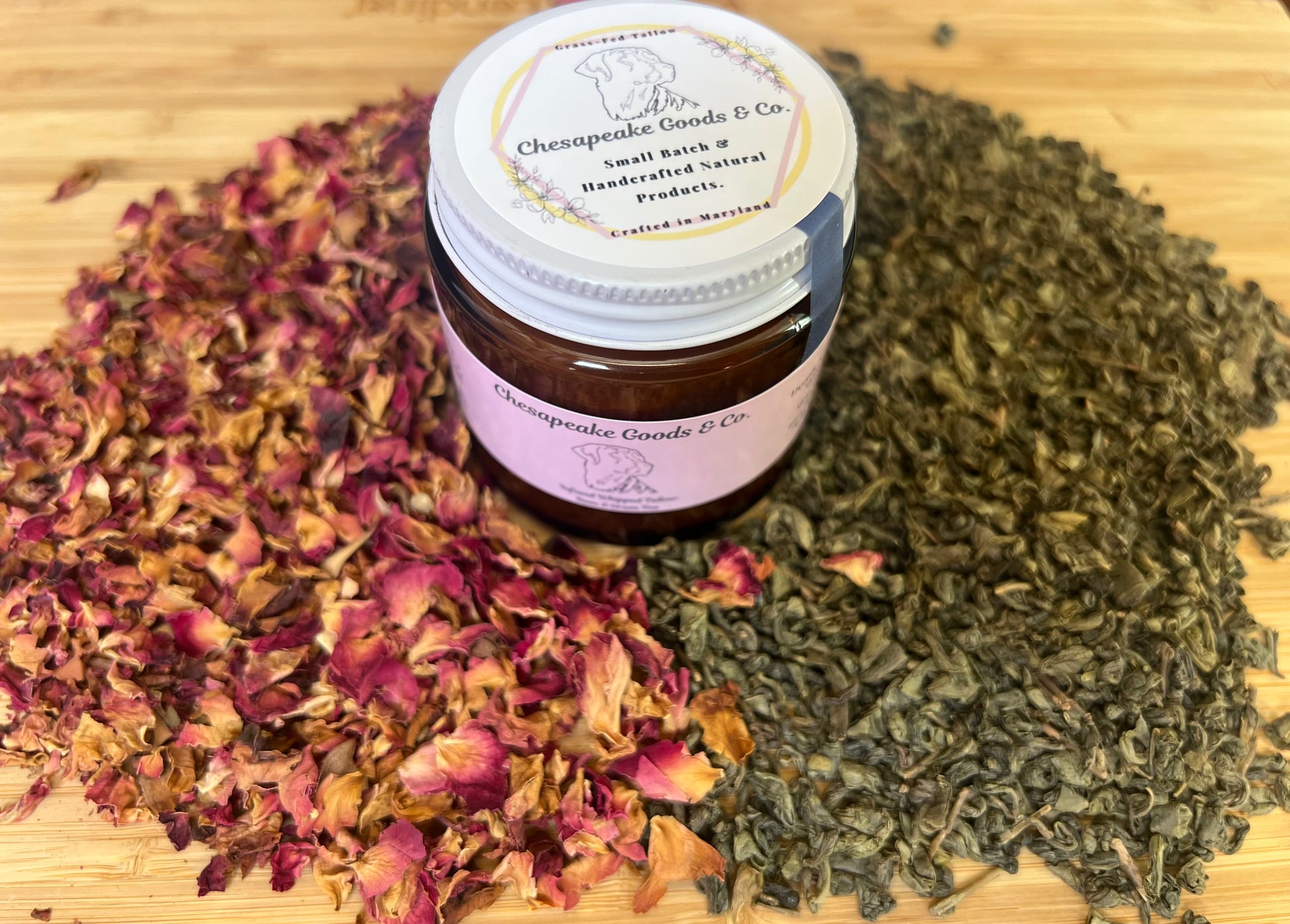 4 oz amber glass jar with pink wrap label and white lid surrounded by dried green tea leaves and rose petals on a wooden surface.