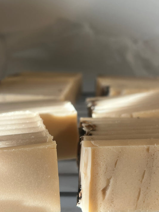 Rows of freshly cut, pale yellow homemade soap bars cool on a wire rack.
