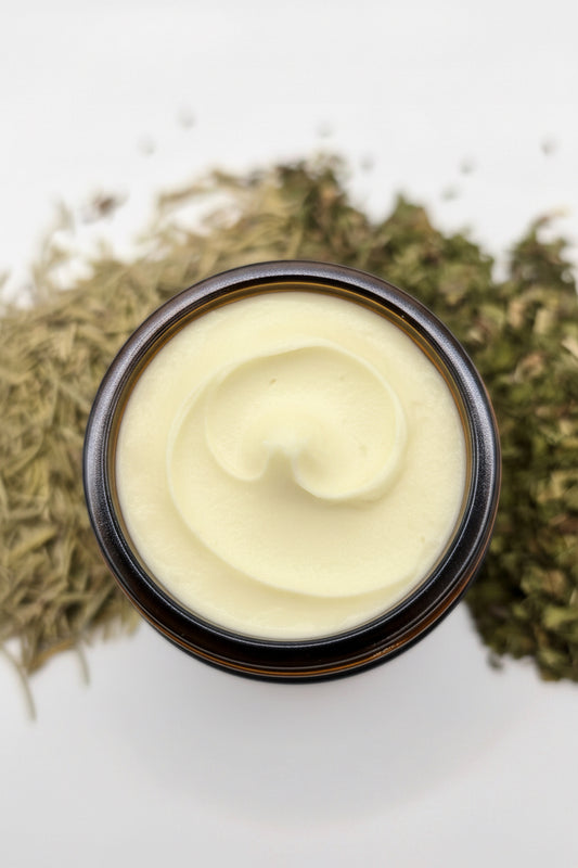 Top-down view shows a jar of herbal whipped balm surrounded by dried peppermint and rosemary herbs.
