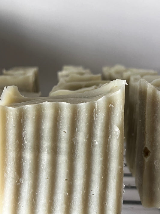 Close-up shows freshly cut, green textured bars of artisan soap cooling on a wire rack.
